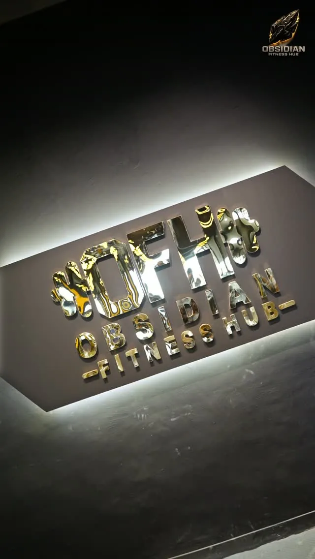 The backlit gold Obsidian Fitness Hub sign on the wall inside the gym.